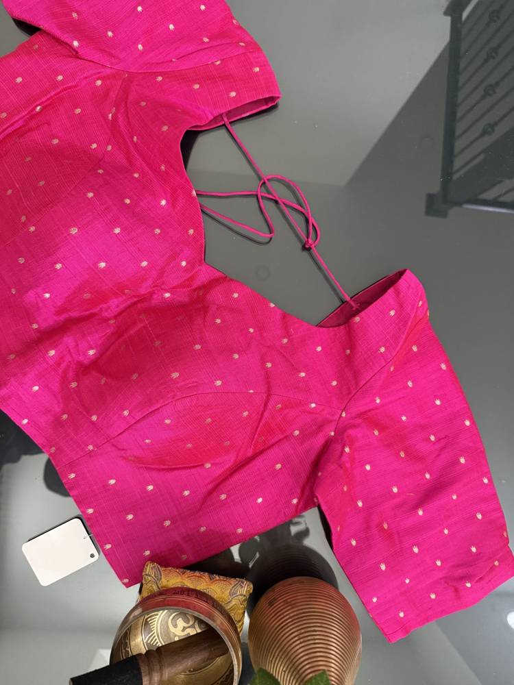 A bright pink cotton blouse with small white polka dots, laid flat on a gray surface with a matching pink tie string.