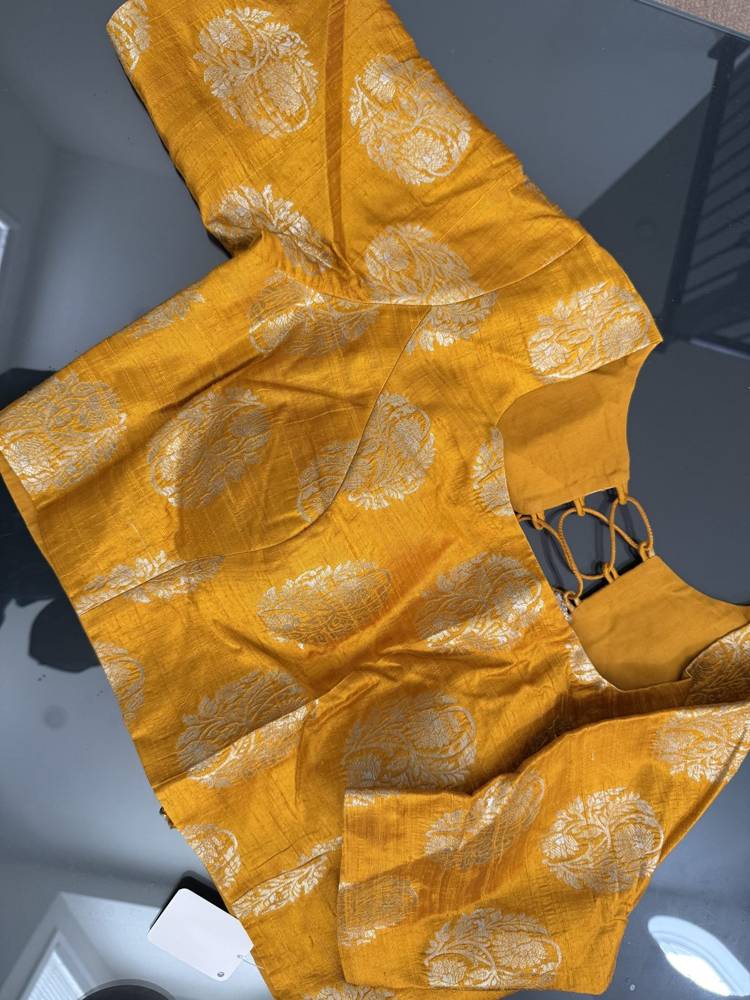 A mustard yellow fabric garment with metallic gold circular motifs, laid flat on a dark gray surface.